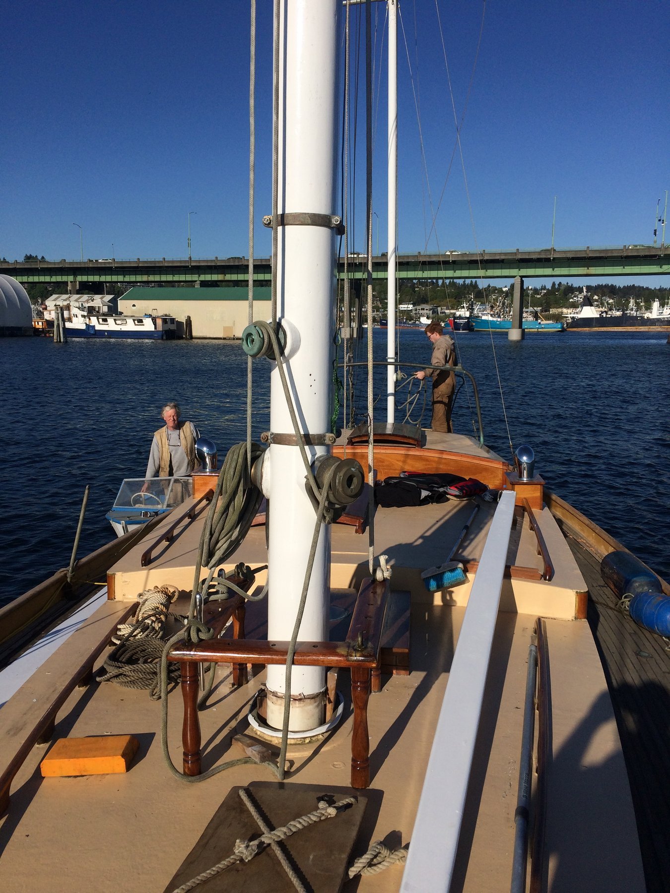 A crew member tends to the boom and rigging of the classic 1946 Merry Maiden, her wooden davits and traditional tackle gleaming in bright Puget Sound sunshine as sister vessels rest nearby at the dock.