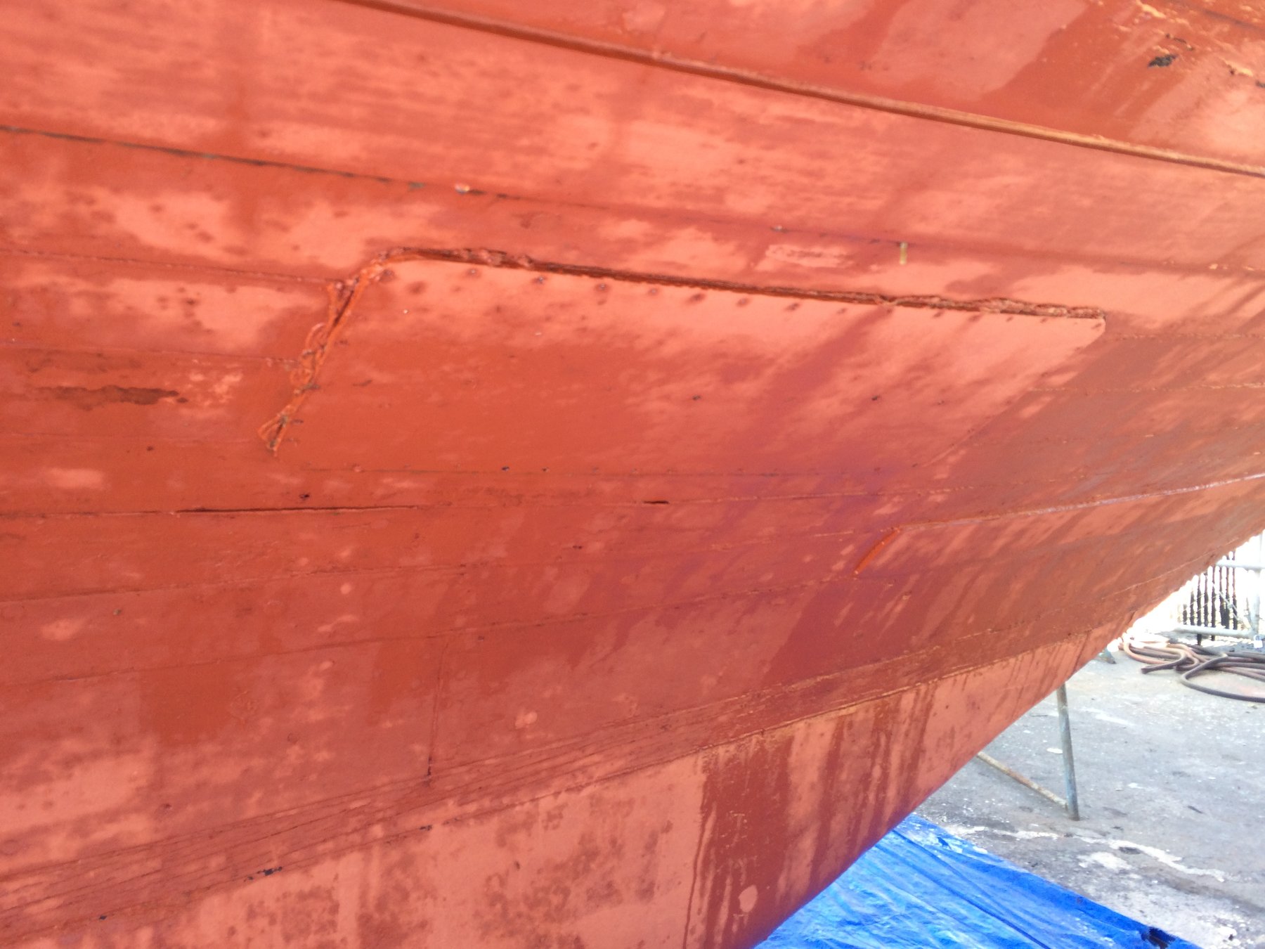 The weathered hull of classic yacht Merry Maiden reveals decades of Pacific Northwest cruising, her red paint worn smooth by salt water and time in Puget Sound.