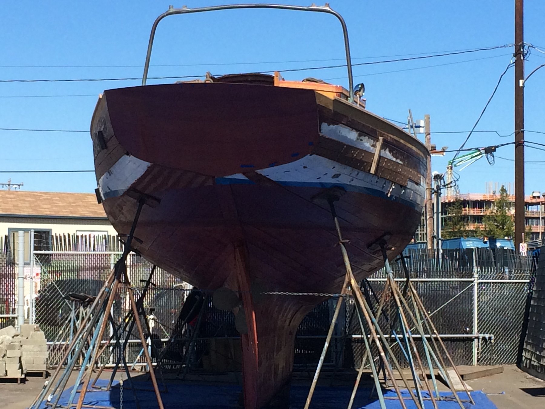 The classic 1946 Philip Rhodes-designed Merry Maiden sits cradled in her boatyard berth, her dark hull supported by wooden shores as she awaits restoration or maintenance in the Puget Sound shipyard.