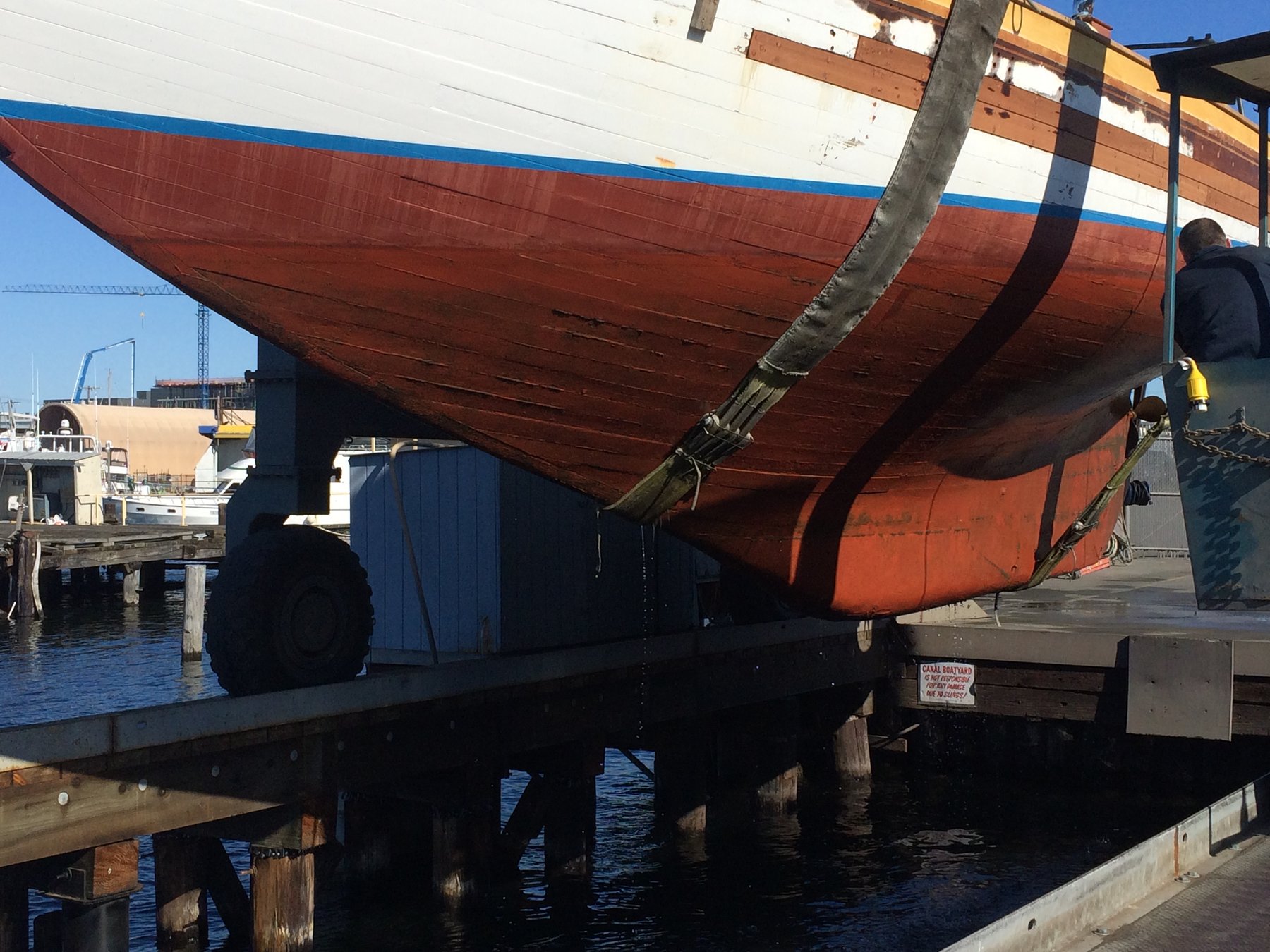 The classic 1946 Philip Rhodes design Merry Maiden rests on the hard at a Puget Sound shipyard, her red hull and white topsides reflecting decades of character alongside the industrial maritime infrastructure.