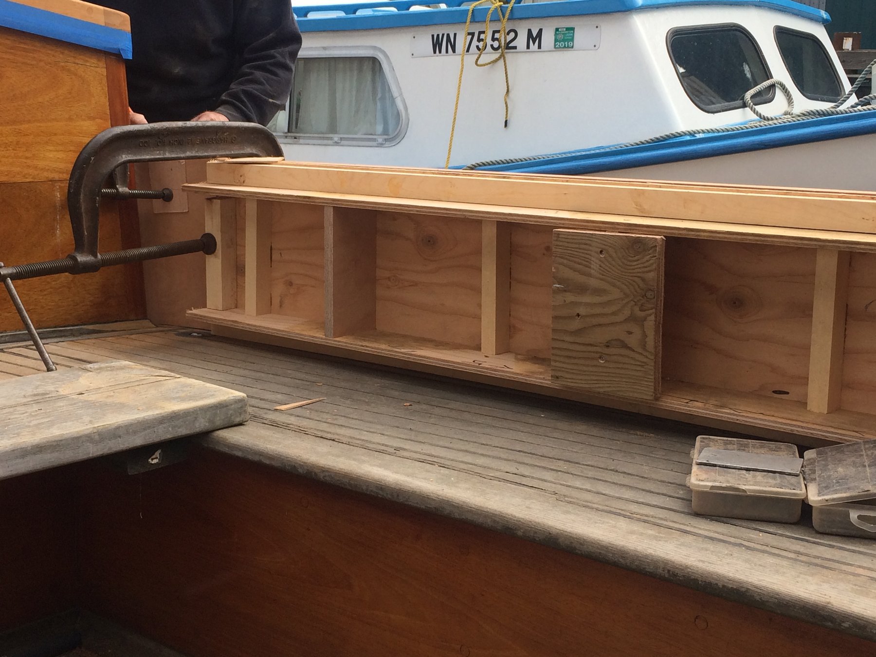 Fresh wooden cabinetry takes shape along the rail of the classic 1946 Philip Rhodes yacht Merry Maiden, with a C-clamp securing the new joinery as restoration work progresses in the Puget Sound boatyard.