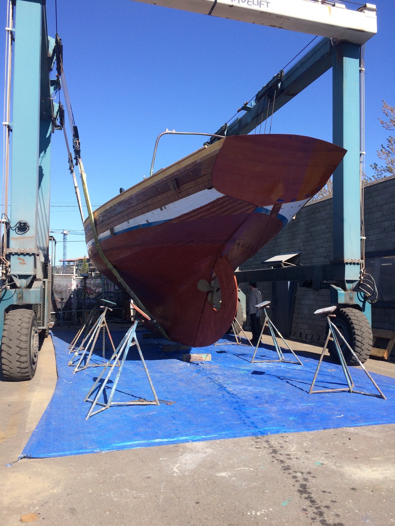 The classic 1946 Philip Rhodes-designed Merry Maiden sits at rest in Puget Sound, her deep burgundy hull and weathered blue canvas catching the brilliant spring sunlight against clear skies.