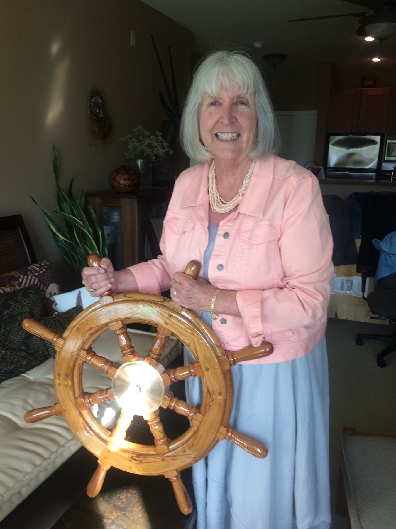 A beaming crew member at the helm of the classic 1946 Philip Rhodes-designed Merry Maiden, displaying the wooden ship's wheel with characteristic pride and joy.