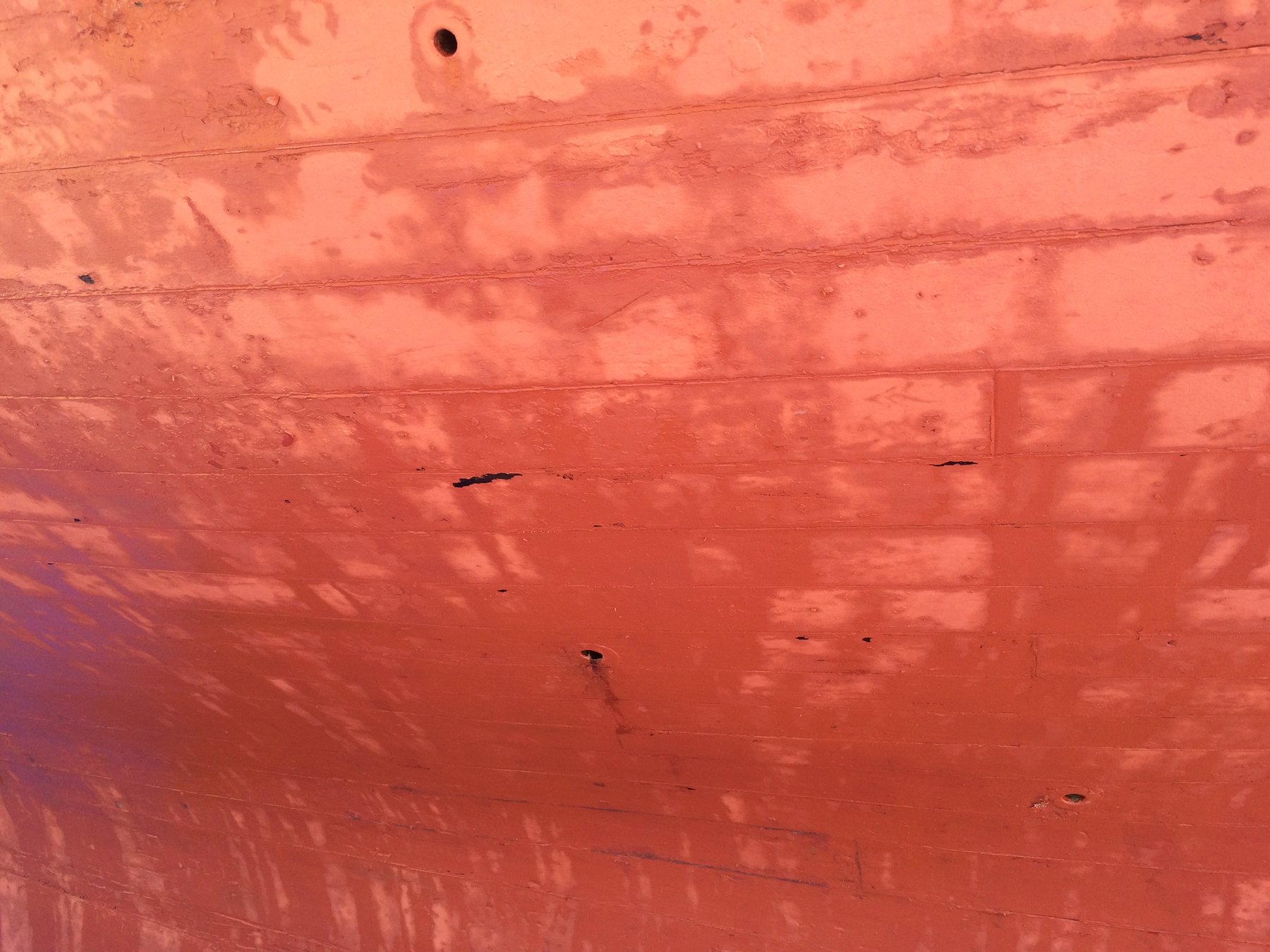 The weathered hull of Merry Maiden reveals the patina of decades—her red-orange paint worn smooth by sun, salt, and time, showing the honest character of a classic wooden yacht that has earned her years.