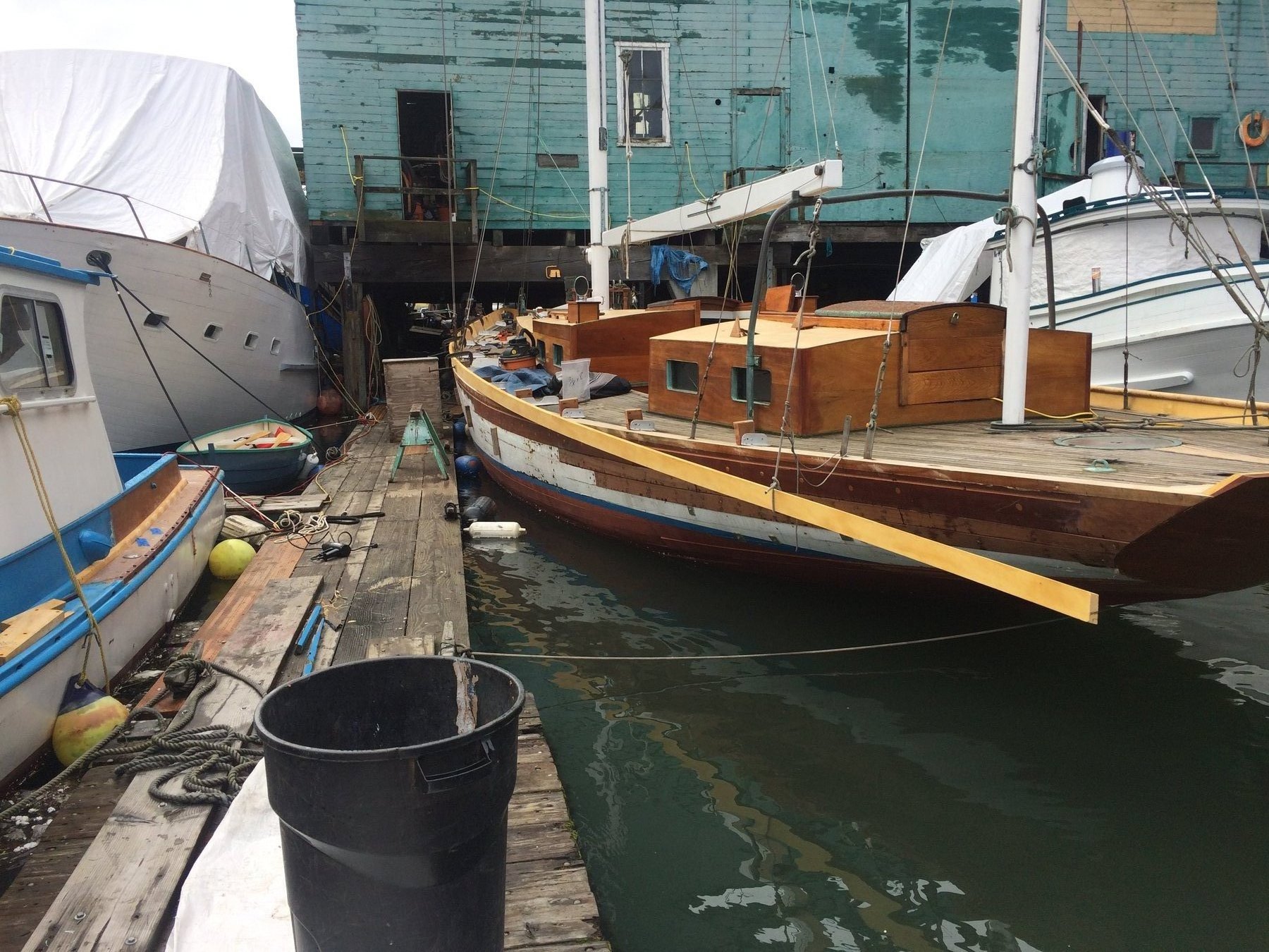 The classic wooden hull of Merry Maiden rests alongside fellow vessels at a Puget Sound marina, her distinctive yellow and blue trim reflecting decades of Pacific Northwest character and heritage.
