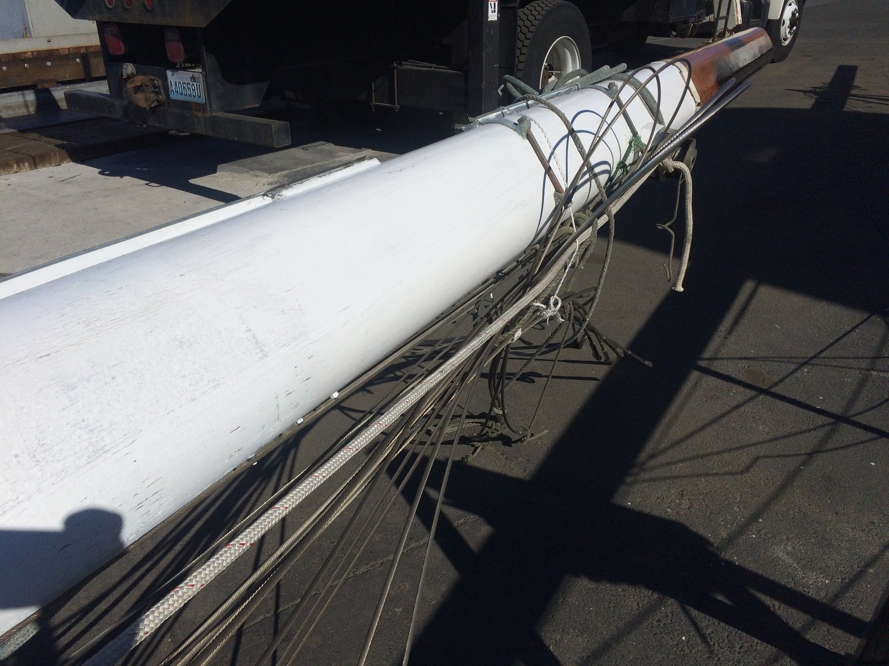 A freshly painted mast lies secured on the hard, its gleaming white surface contrasting sharply with the industrial boatyard setting—a testament to the ongoing restoration of this classic 1946 Philip Rhodes design in the Puget Sound.