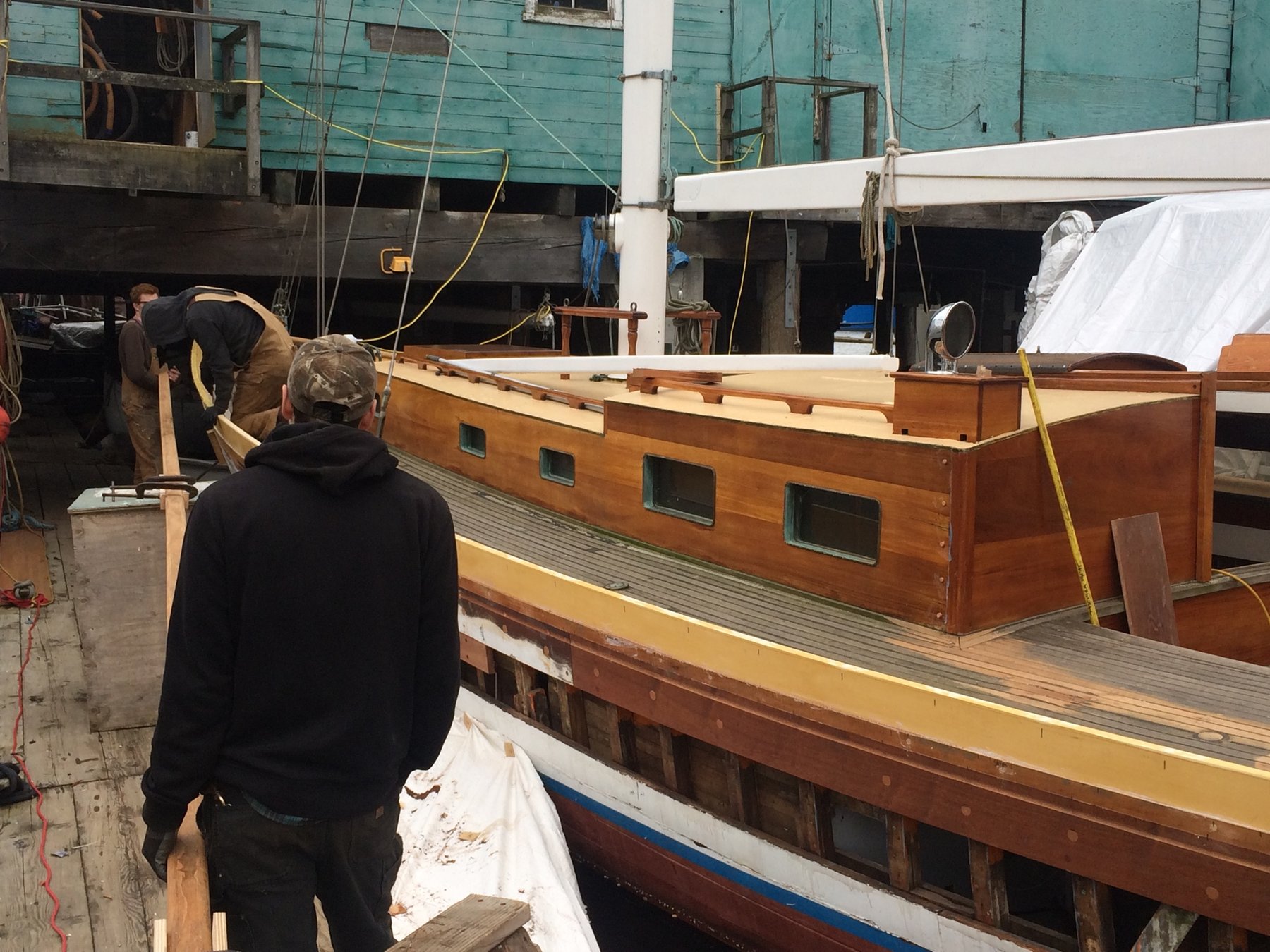 Skilled craftsmen work on the wooden hull of the classic 1946 Merry Maiden in the boatyard, preserving the elegant lines of this Philip Rhodes design through meticulous restoration work.