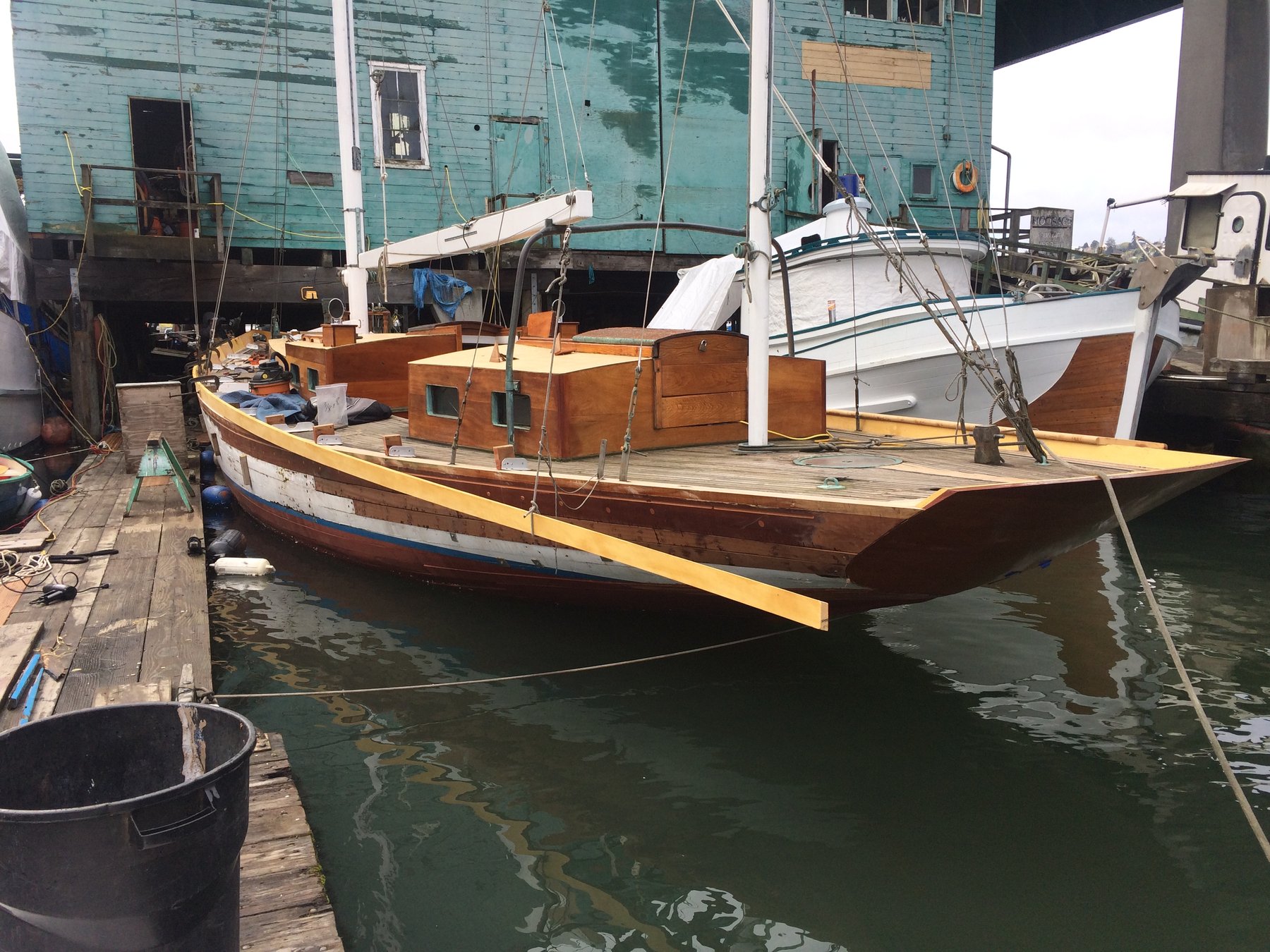 The classic 1946 Philip Rhodes-designed Merry Maiden rests peacefully at her Puget Sound moorage, her warm wood tones and traditional lines reflecting timeless craftsmanship against the industrial backdrop of a working maritime district.
