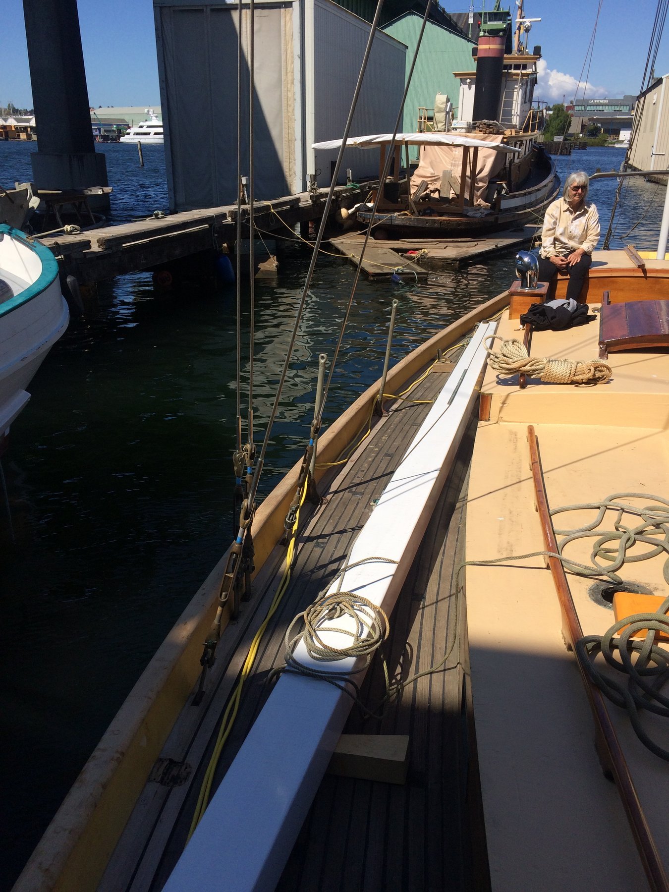 The classic 1946 Philip Rhodes-designed Merry Maiden rests at her moorings in Puget Sound, her graceful wooden hull and traditional rigging catching the afternoon light against the industrial backdrop of the Pacific Northwest.