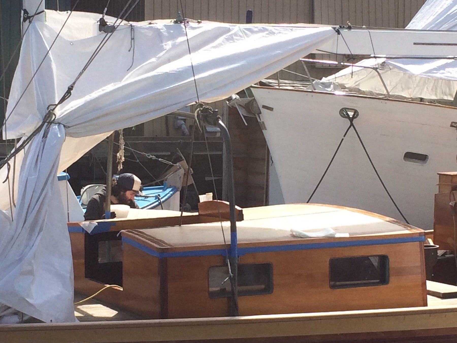 A crew member tends to the Merry Maiden's bright white sails during maintenance, with the classic wooden hull and blue trim gleaming in Puget Sound sunshine. This 1946 Philip Rhodes design shows the meticulous care required to keep a vintage sailboat in sailing condition.