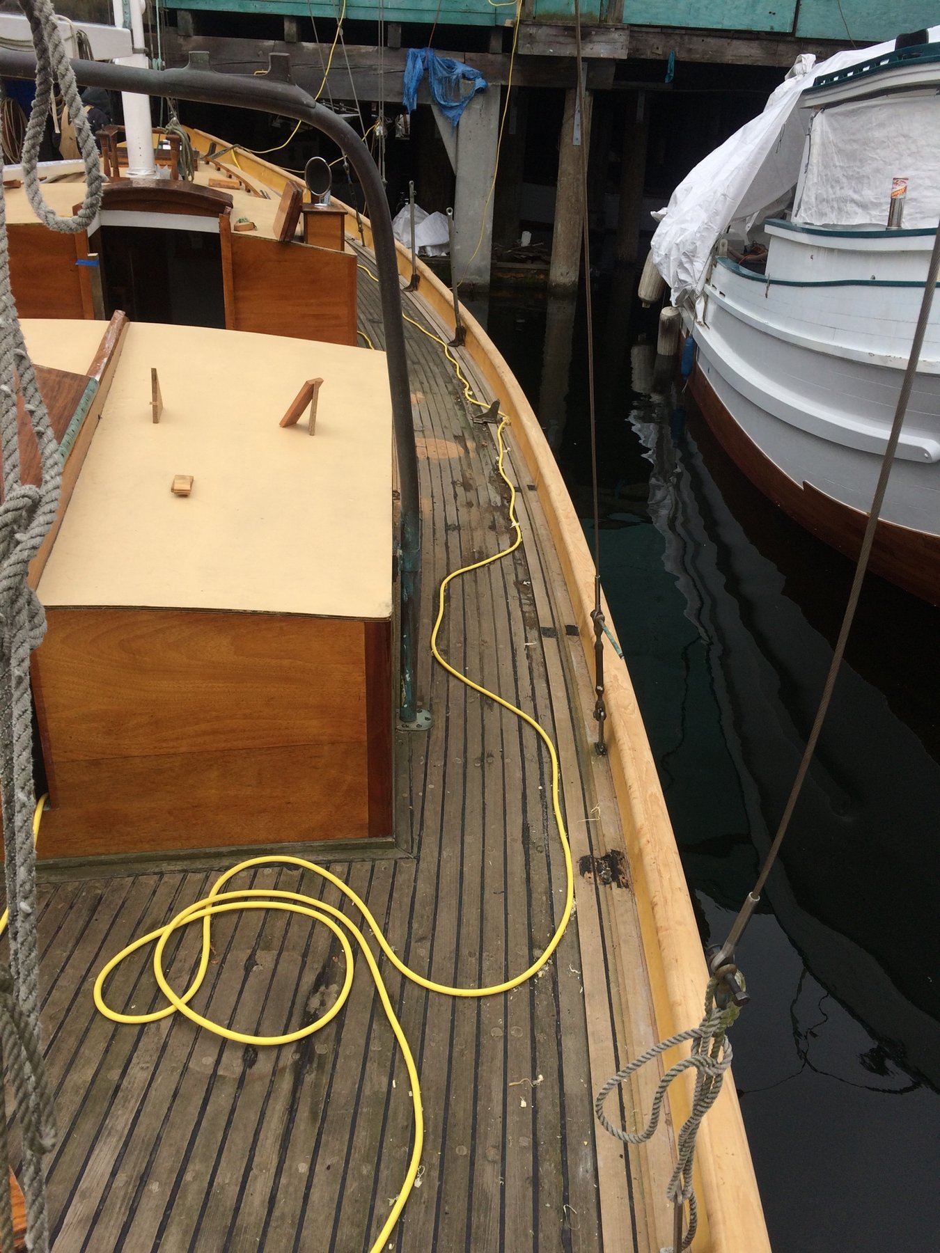 Merry Maiden's teak deck gleams in spring sunlight as the classic 1946 Rhodes design sits moored alongside her neighbors, yellow shore power cord snaking across her meticulously maintained surface.
