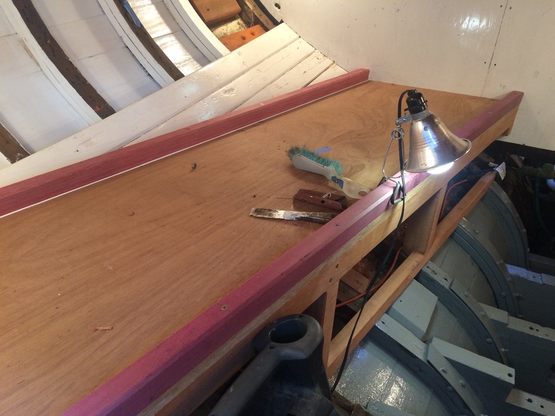 Work-in-progress restoration of Merry Maiden's cabin, with work lamp illuminating the wooden interior as craftspeople tend to the classic 1946 yacht's woodwork and fittings.