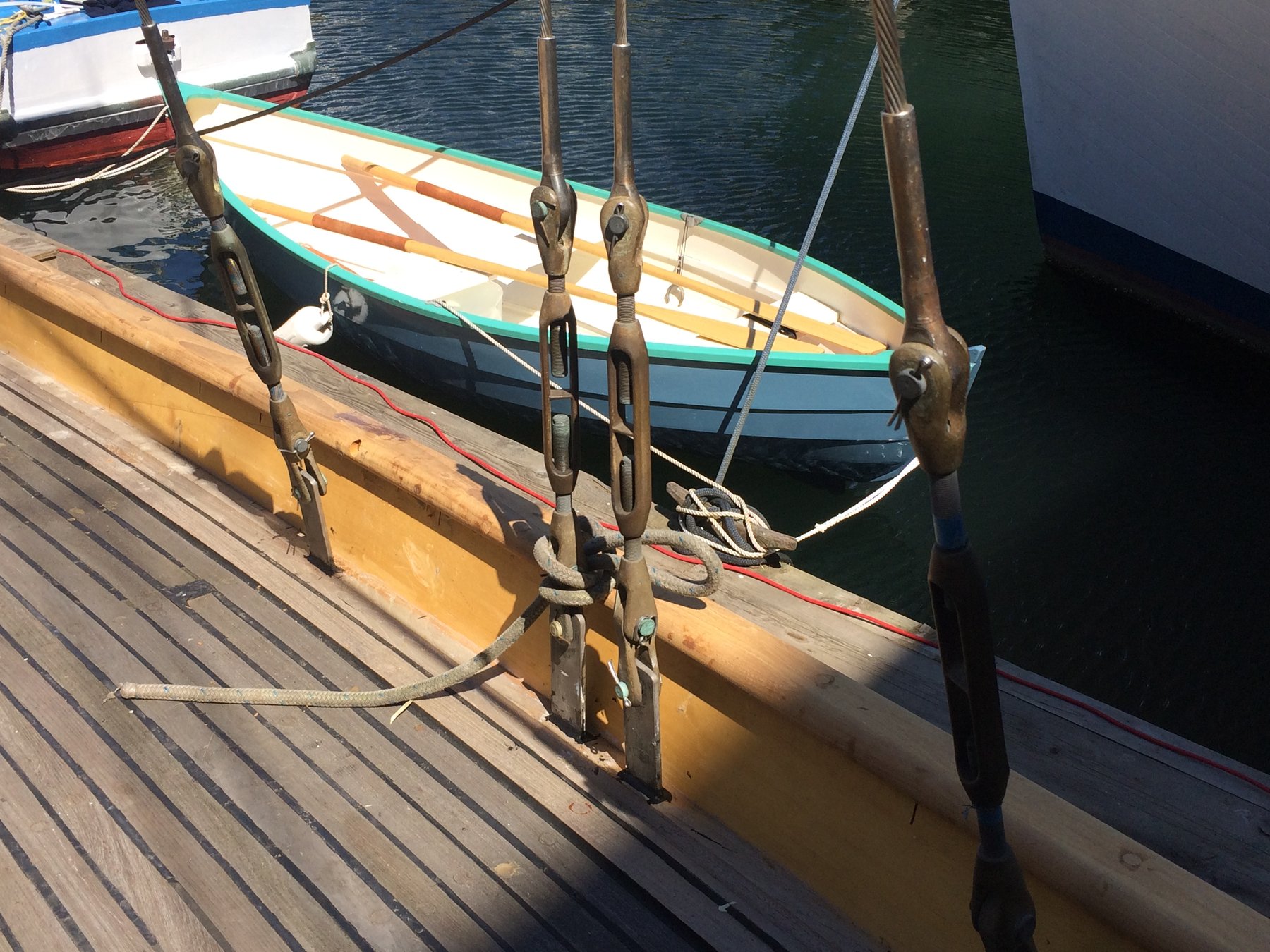 The Merry Maiden's weathered wooden hull and bronze rigging rest peacefully at the dock in Puget Sound, her classic 1946 lines reflected in the still waters alongside a colorful neighbor.