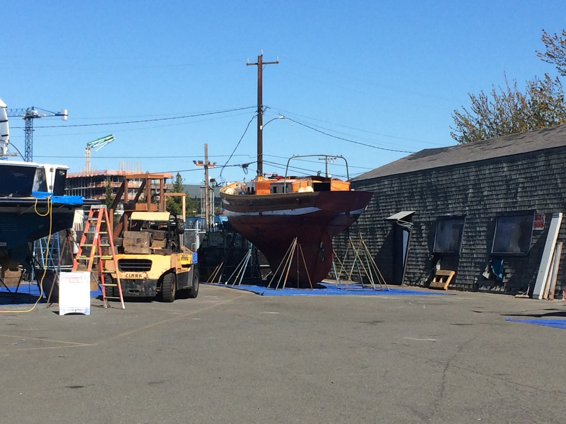 The classic 1946 Philip Rhodes-designed Merry Maiden rests in the boatyard on the hard, surrounded by restoration equipment and timber supports in the Puget Sound shipyard.