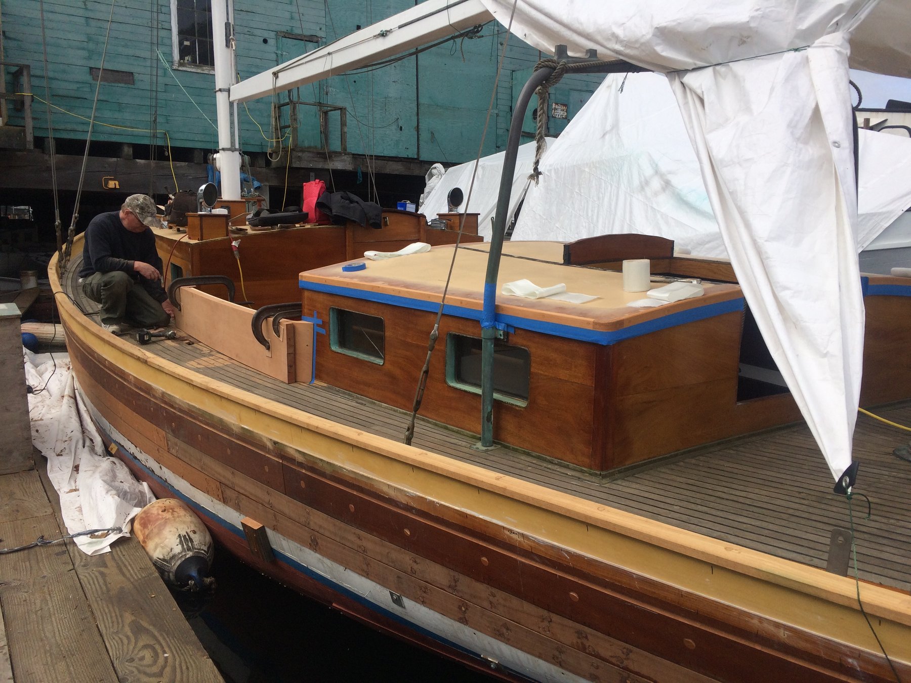 A craftsman tends to the classic lines of Merry Maiden, a 1946 Philip Rhodes design, as white canvas awnings provide shelter on her sun-dappled deck in the Puget Sound.