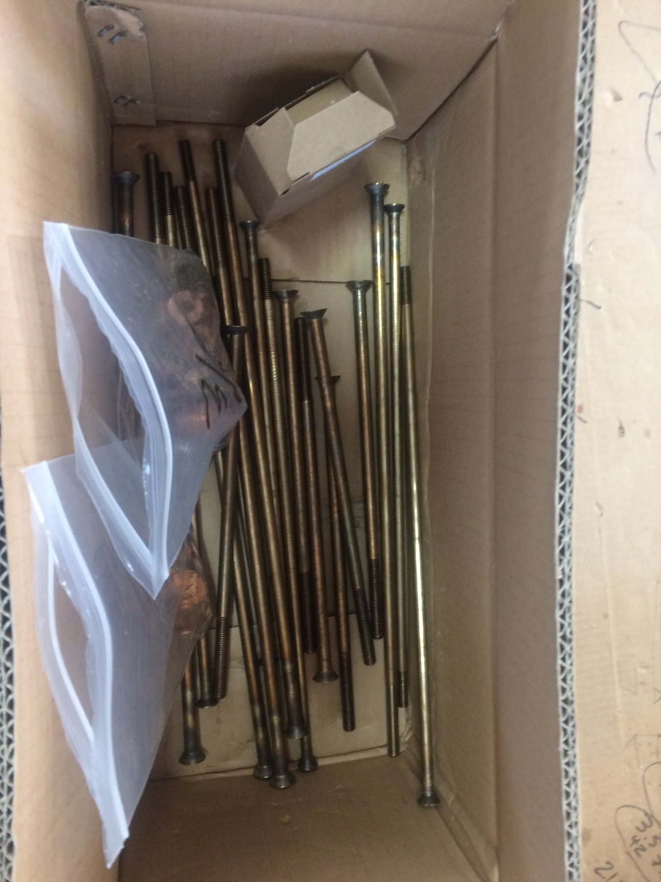A collection of bronze through-hull fittings and stainless steel fasteners awaits installation during restoration work on the classic 1946 Philip Rhodes-designed Merry Maiden, displayed in a cardboard box in the Pacific Northwest.