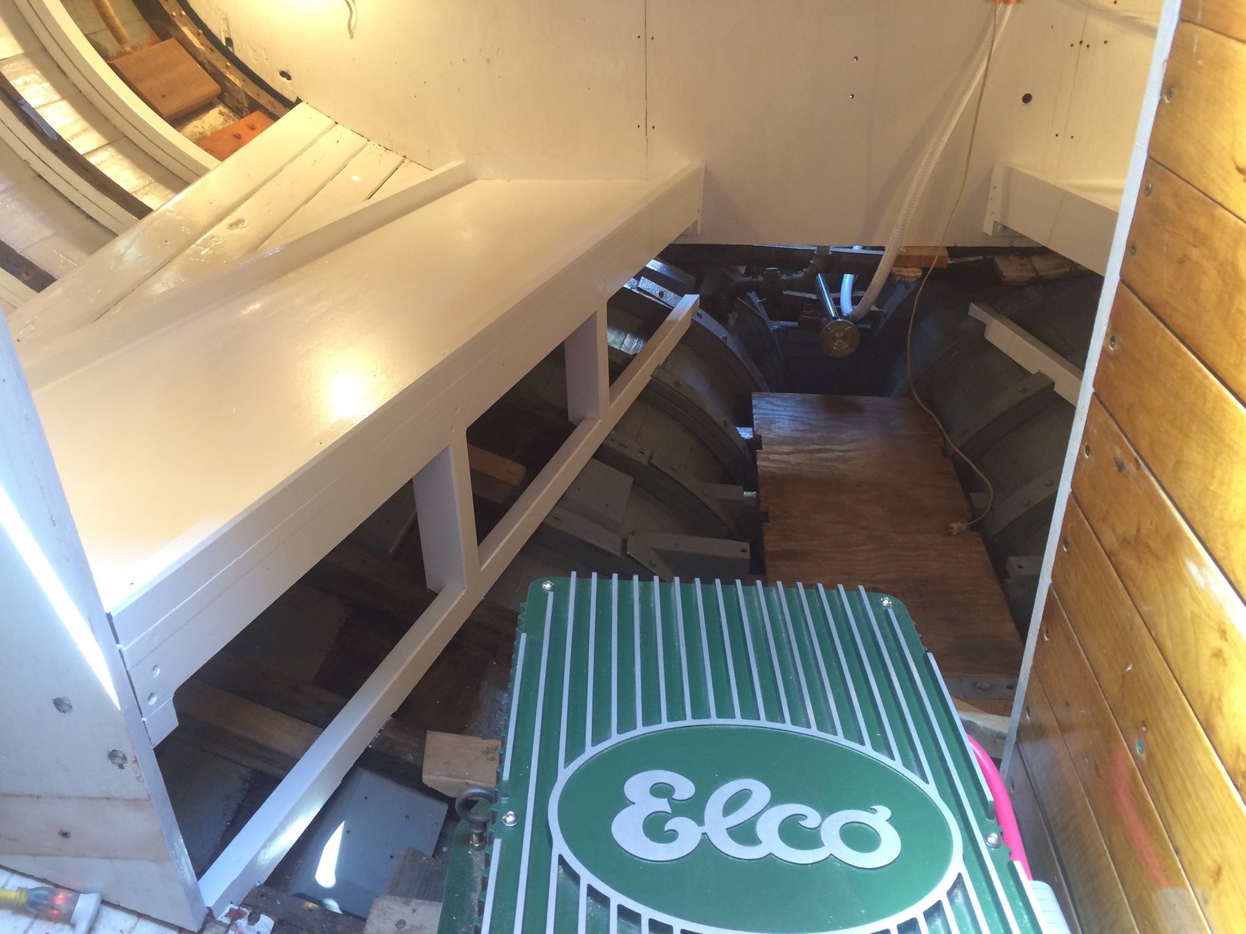 Below deck in Merry Maiden's cabin, white cabinetry and wooden hull frames reveal the classic 1946 construction of this Philip Rhodes design, with an Elco engine cover visible in the companionway.