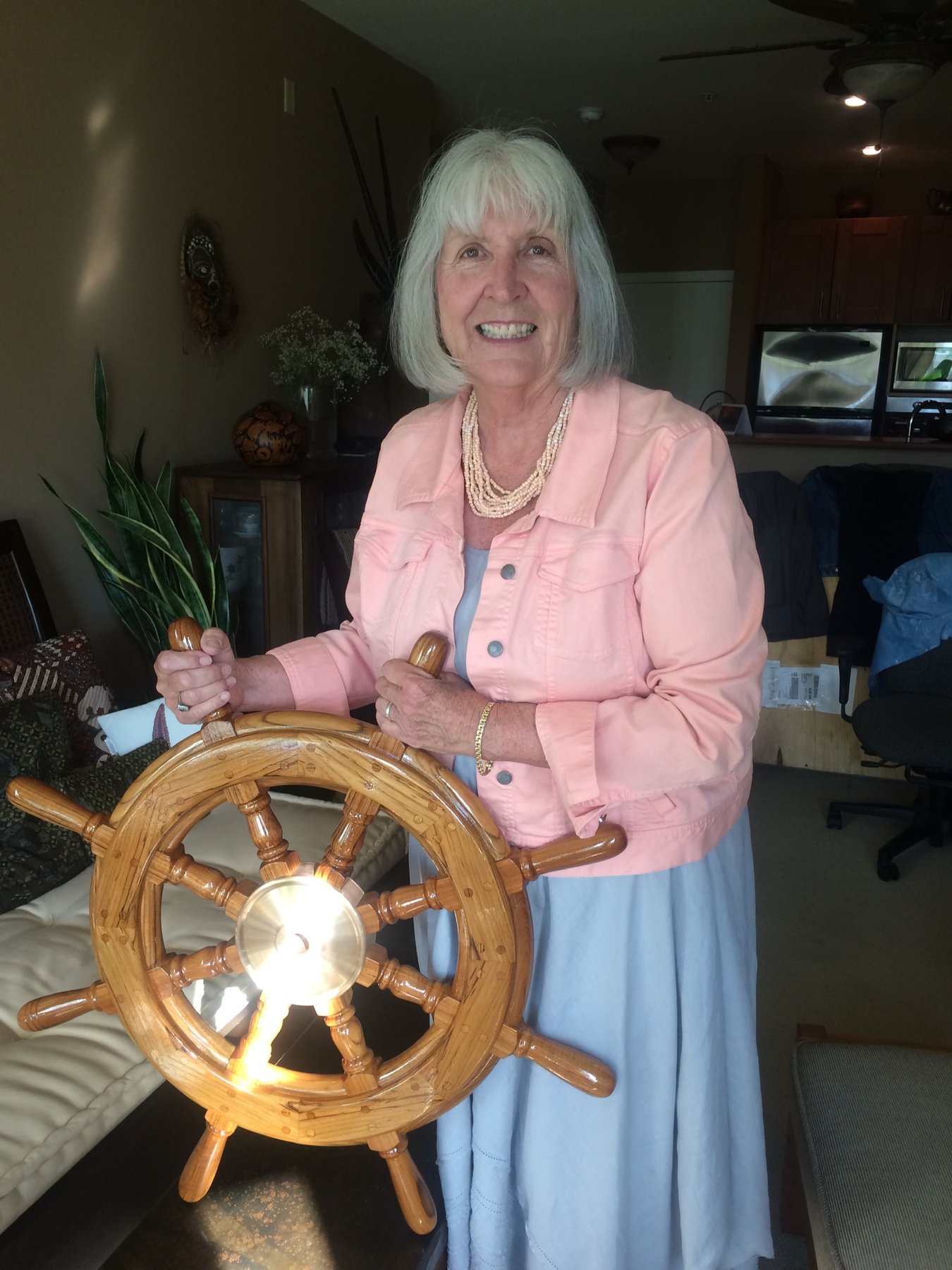 A smiling crew member proudly displays the wooden ship's wheel of the classic 1946 Philip Rhodes-designed Merry Maiden, docked in Puget Sound.