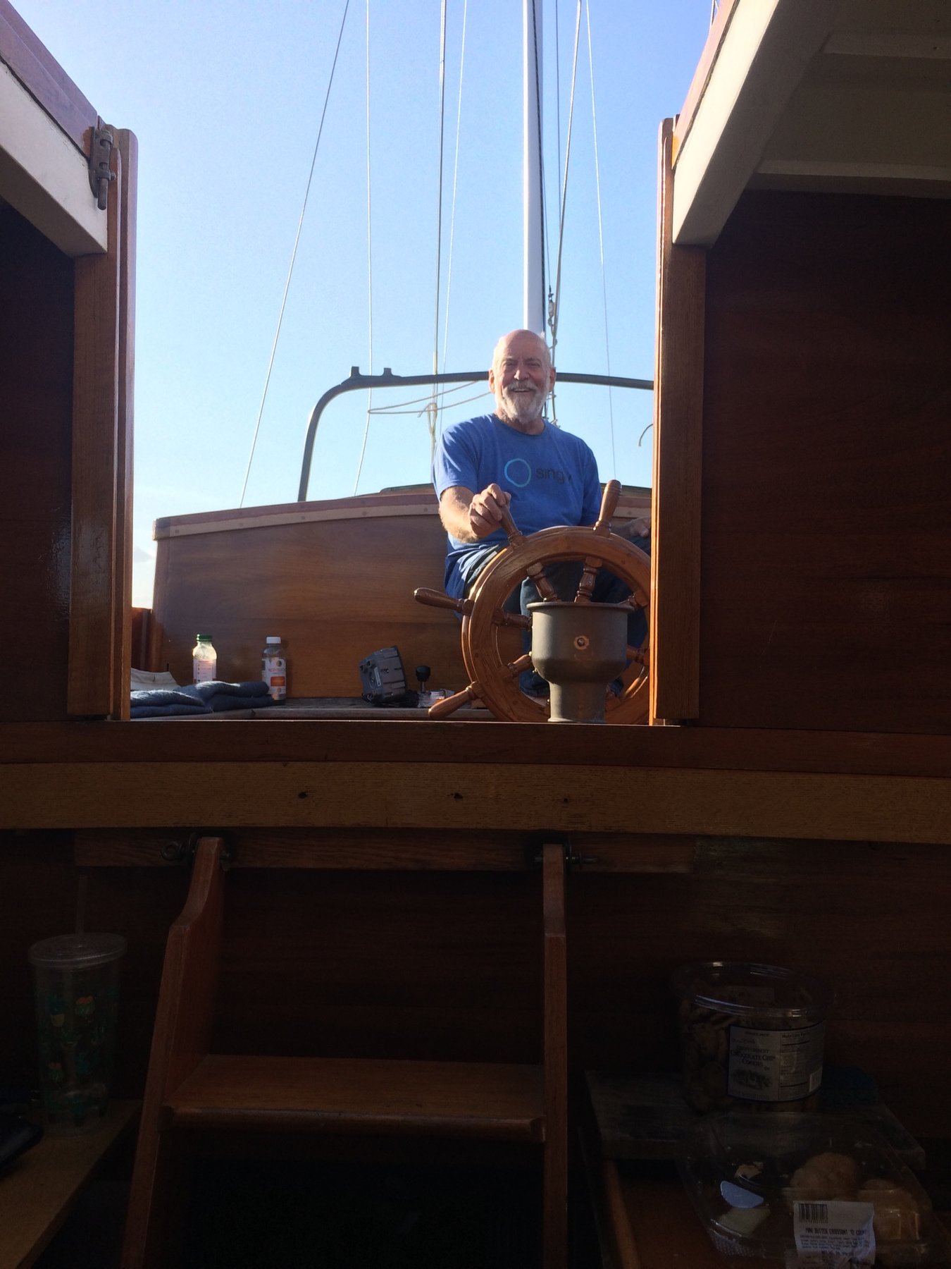 Captain at the helm of Merry Maiden, the classic 1946 Philip Rhodes design, commanding the wooden wheel under clear skies in Puget Sound waters.