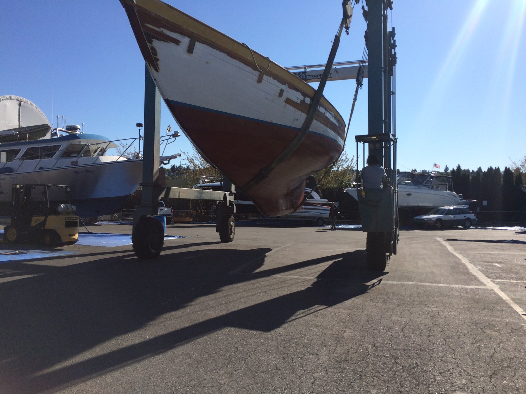 The classic 1946 Philip Rhodes-designed Merry Maiden suspended in the travel lift at a Pacific Northwest boatyard, her wooden hull and graceful lines on full display during haul-out.