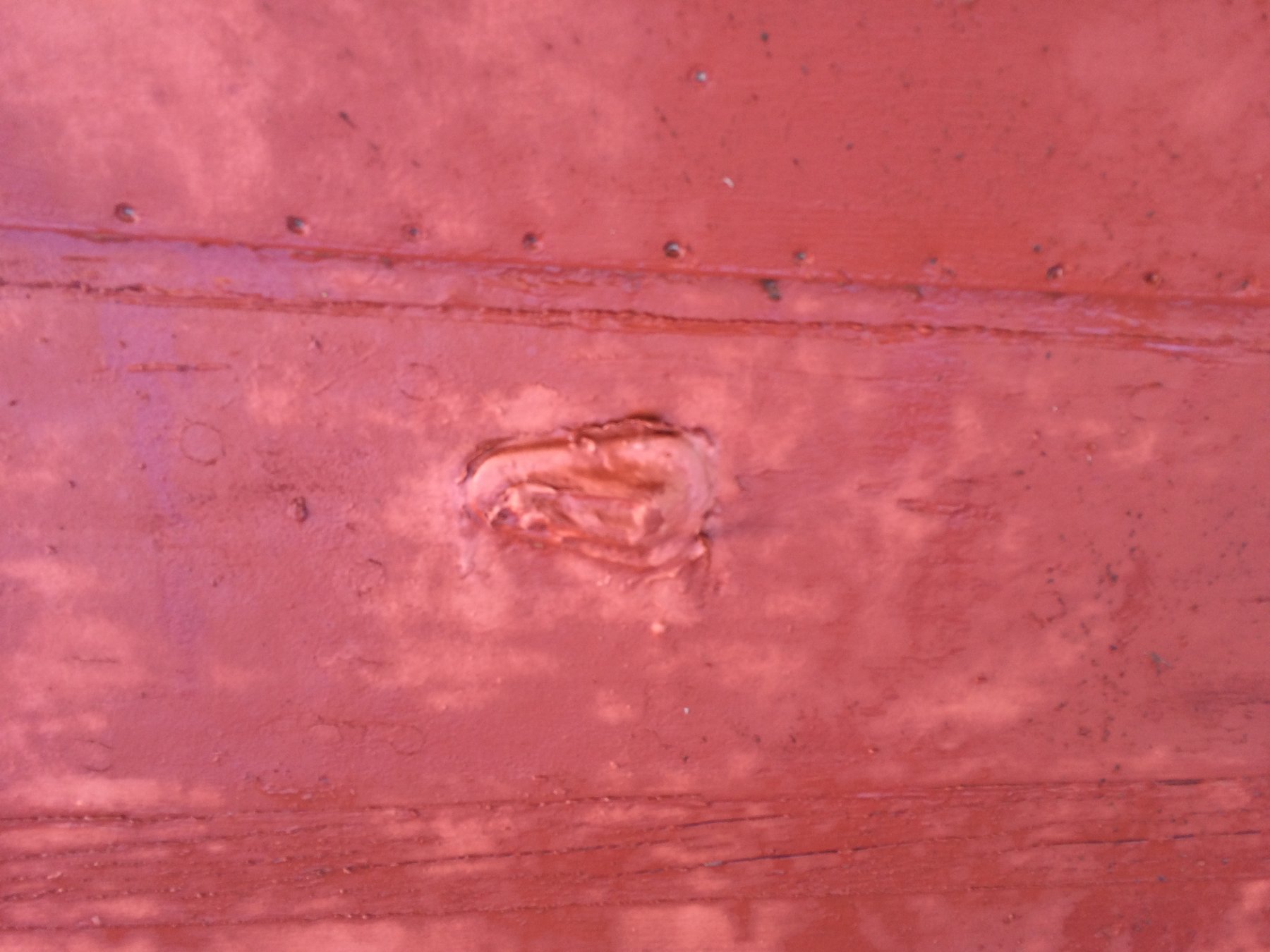 A wooden hull shows its character in faded red paint and weathered surface, with a carefully carved porthole revealing the craftsmanship of this 1946 classic.