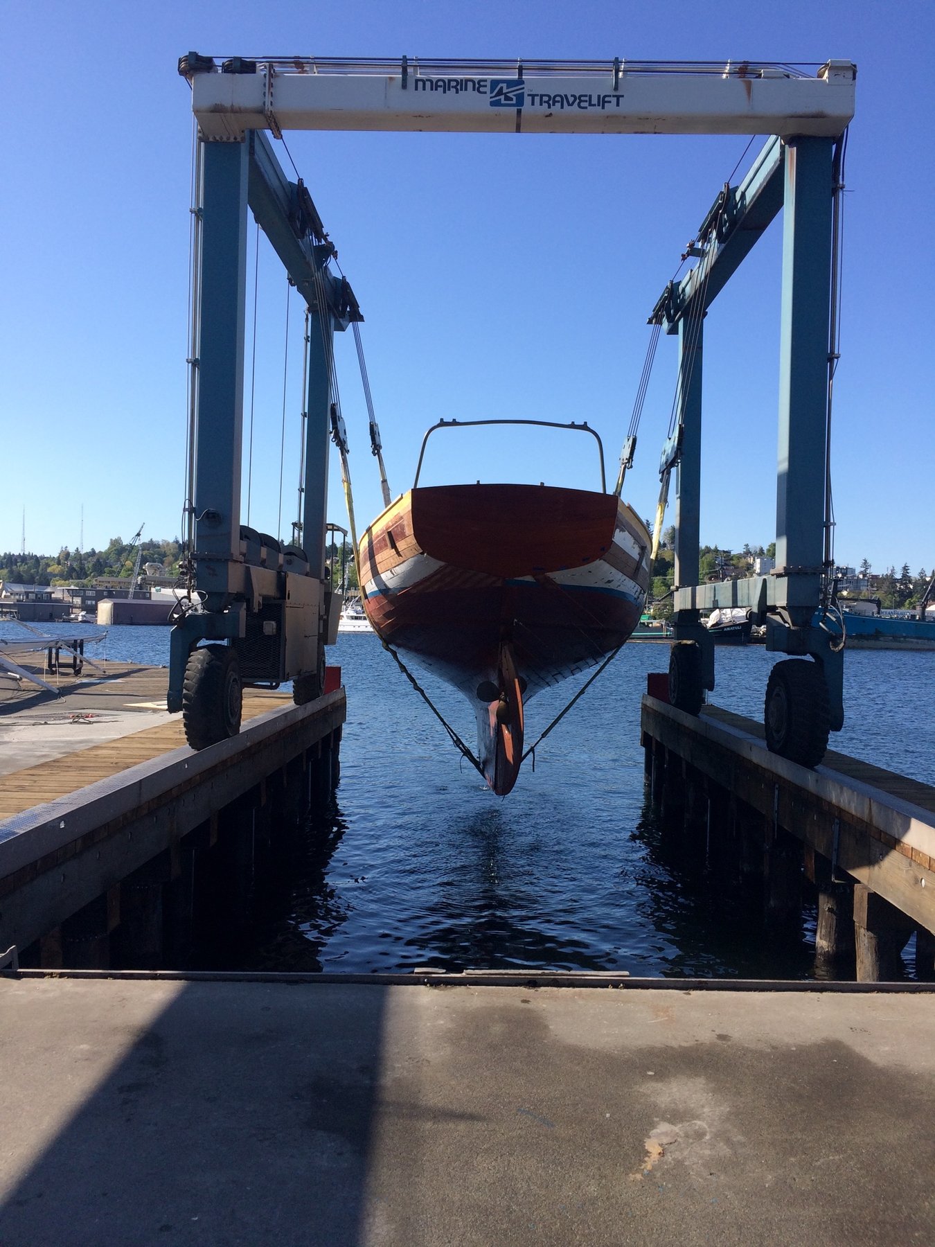 The classic 1946 Philip Rhodes-designed Merry Maiden suspended in the Marine Travelift, her varnished hull gleaming in the spring sunshine as she awaits service in the boatyard.