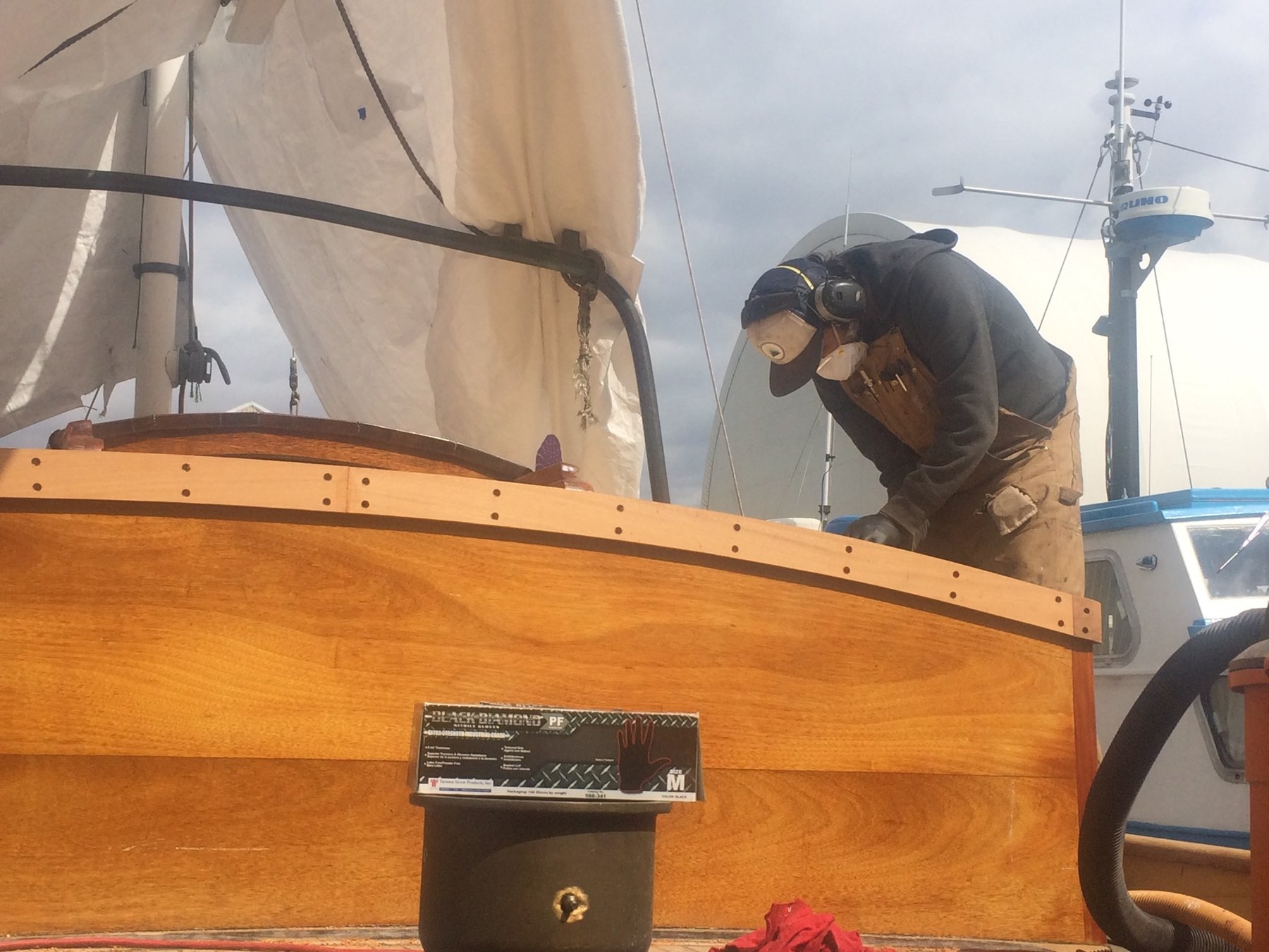 A crew member tends to the varnished teak rail of the classic 1946 Merry Maiden, her traditional canvas sails billowed overhead in steady wind.