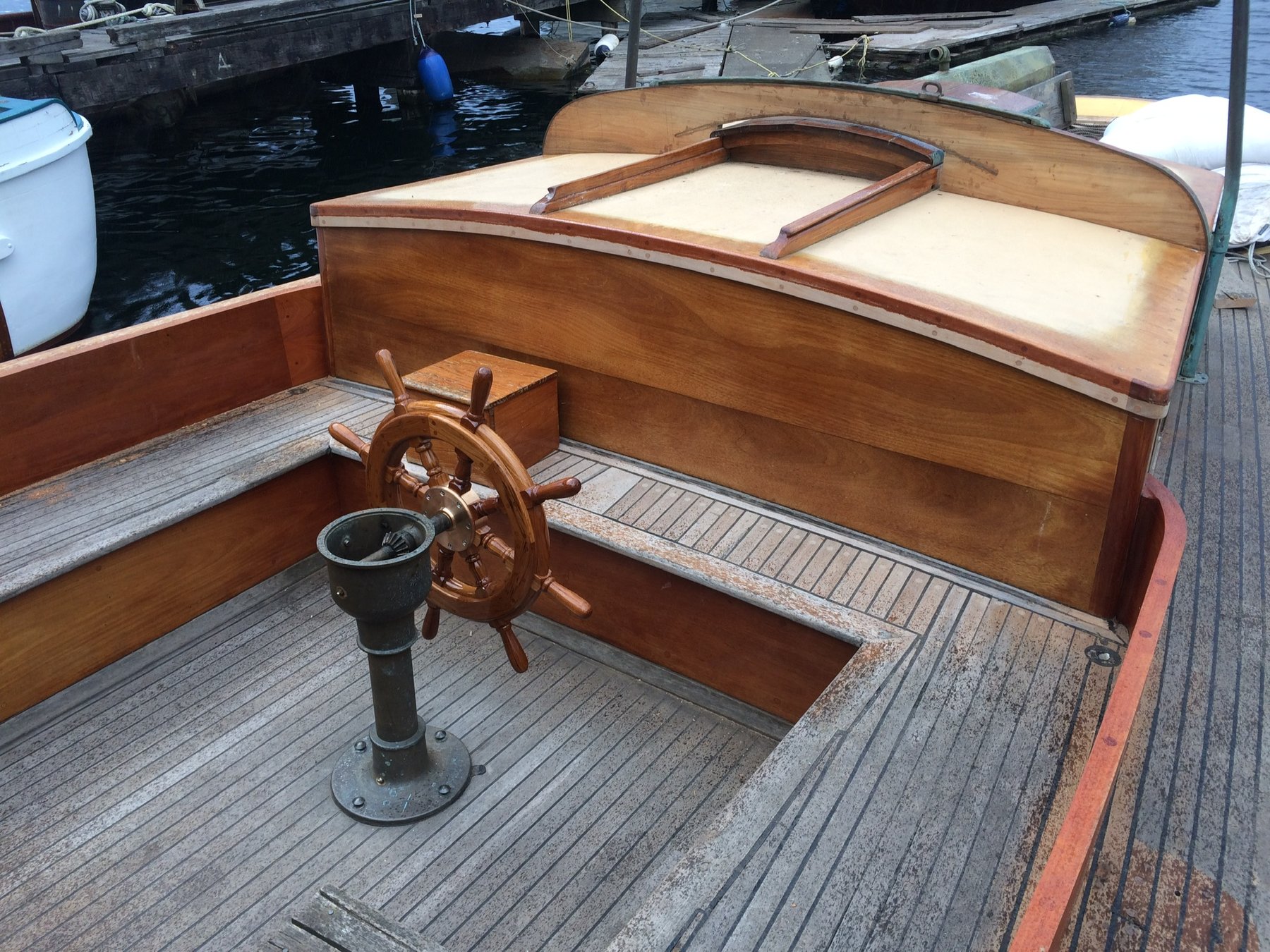 The helm of Merry Maiden, a 1946 Philip Rhodes classic, gleams with polished mahogany and brass fittings while moored in Puget Sound, showcasing the timeless elegance of mid-century yacht craftsmanship.