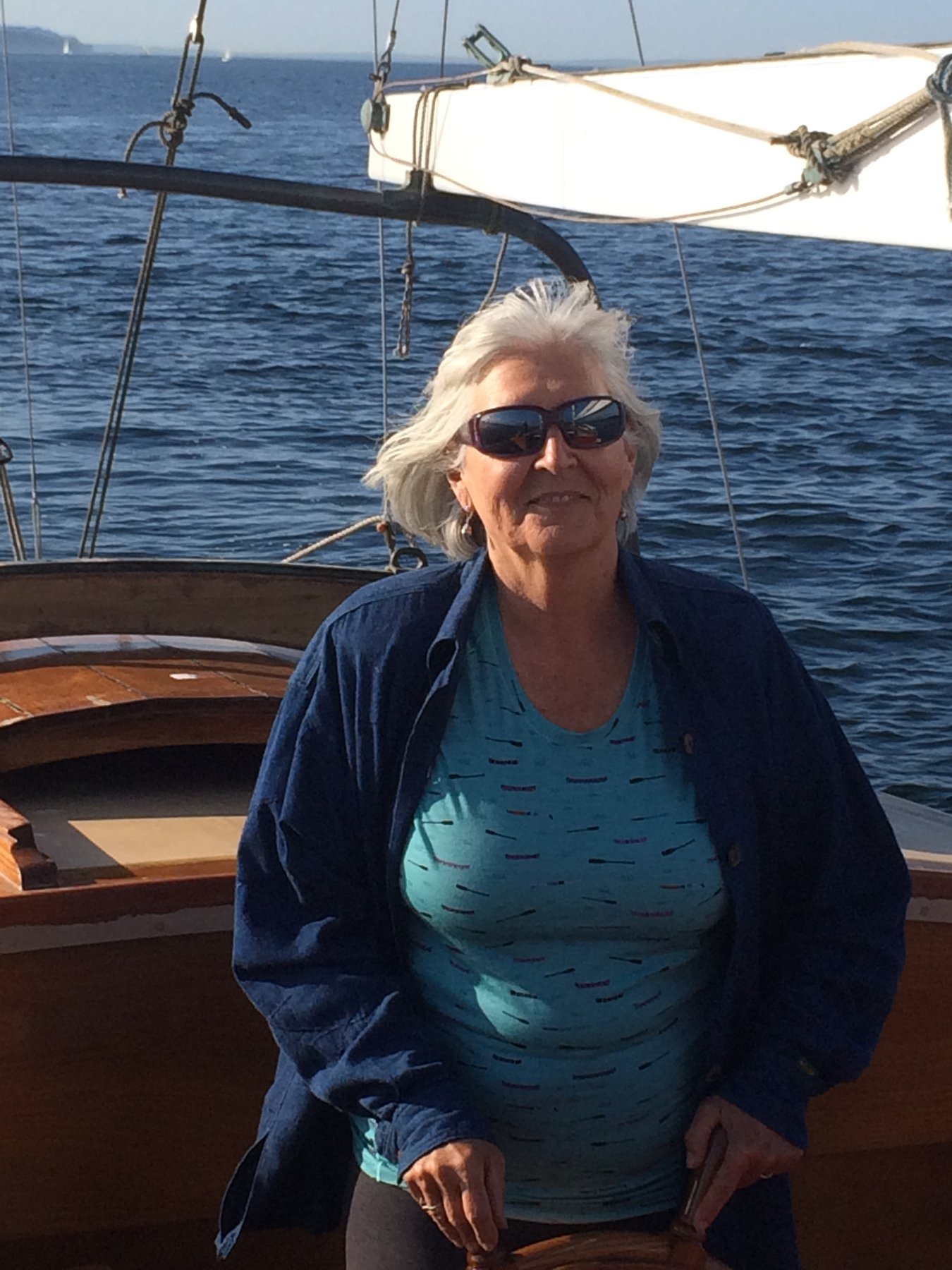 A crew member enjoys the warm sunshine aboard the classic 1946 Philip Rhodes-designed Merry Maiden, with Puget Sound's calm blue waters stretching behind her.
