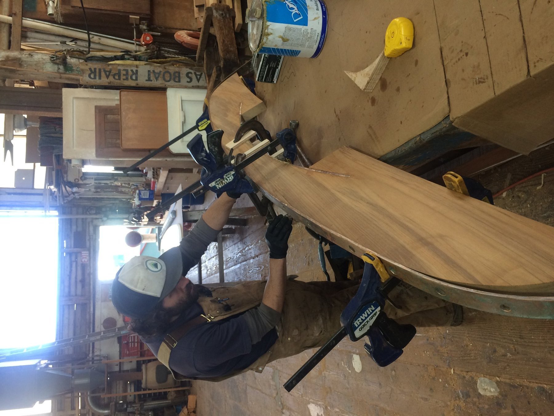A craftsman carefully clamps a wooden plank during restoration work on the classic 1946 Philip Rhodes-designed Merry Maiden, preserving the traditional boatbuilding heritage of this 35-foot sailing yacht.