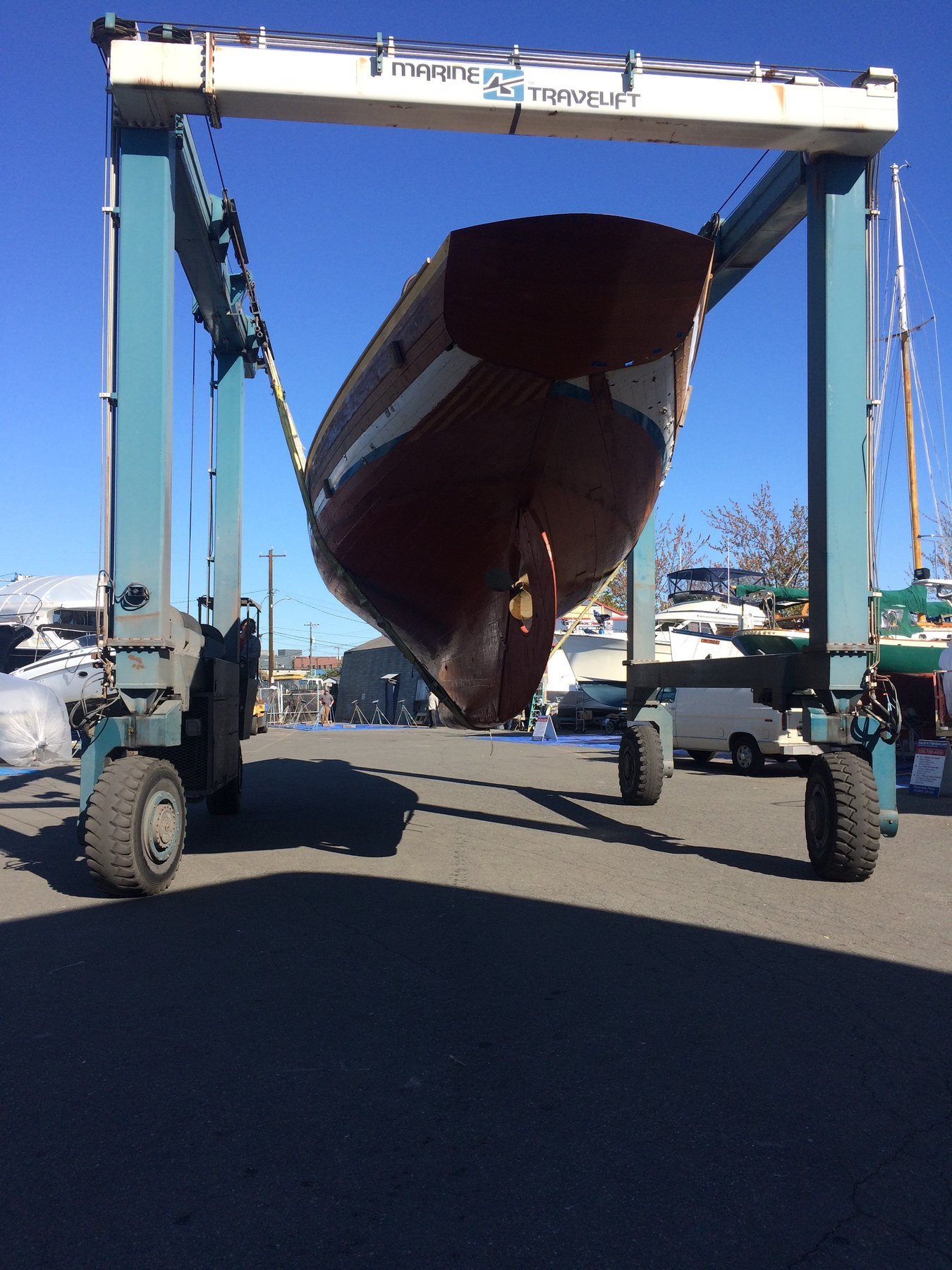 The classic 1946 Philip Rhodes-designed Merry Maiden suspended in the boatyard crane, her mahogany hull gleaming against the clear Puget Sound sky during maintenance.